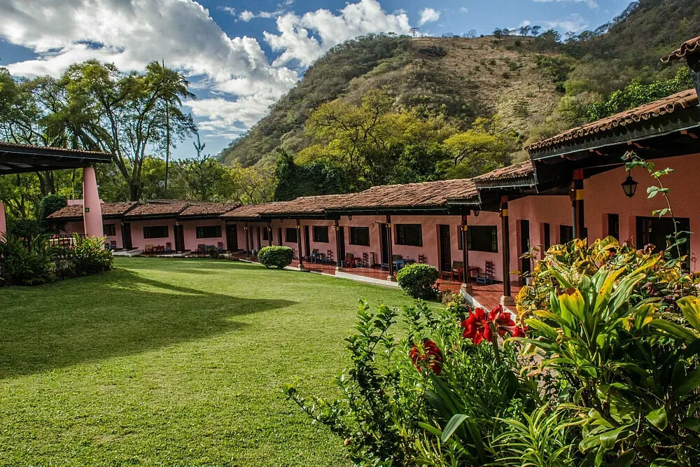Hotel Agua Blanca — The hotel is set within a vibrant tropical canyon, where legendary hot springs flow freely. Lush gardens surround the property, offering verdant views and a sense of immersion in nature. The atmosphere is one of peaceful tranquility, enhanced by the natural sounds of the springs and the abundant plant life.