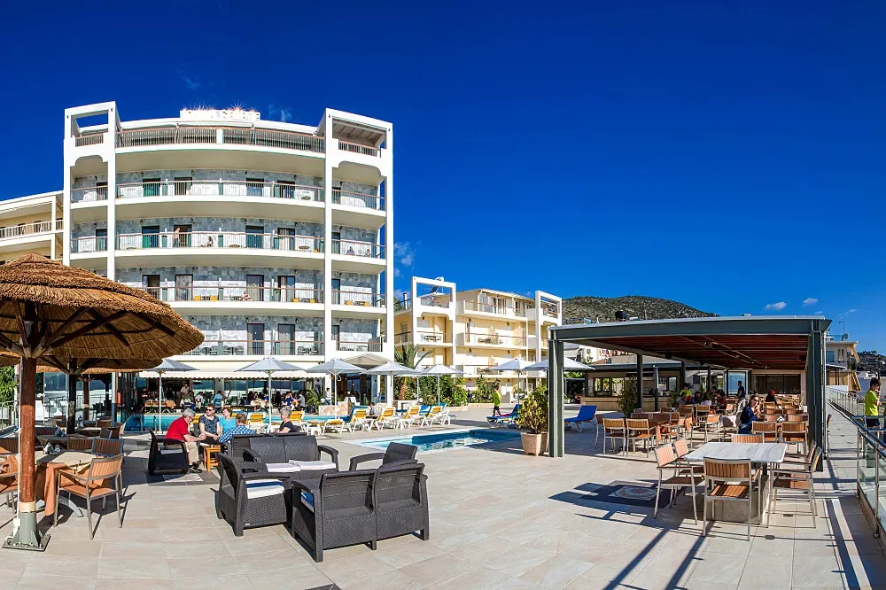 JOHN & GEORGE — The John & George hotel is situated in the historic part of Tolo, providing an exceptional vantage point over the bay. The landscape is dominated by the picturesque islands of Romvi and Koronisi, complemented by the activity of a working harbor with cruise ships and fishing boats. This coastal environment offers a serene yet engaging atmosphere.