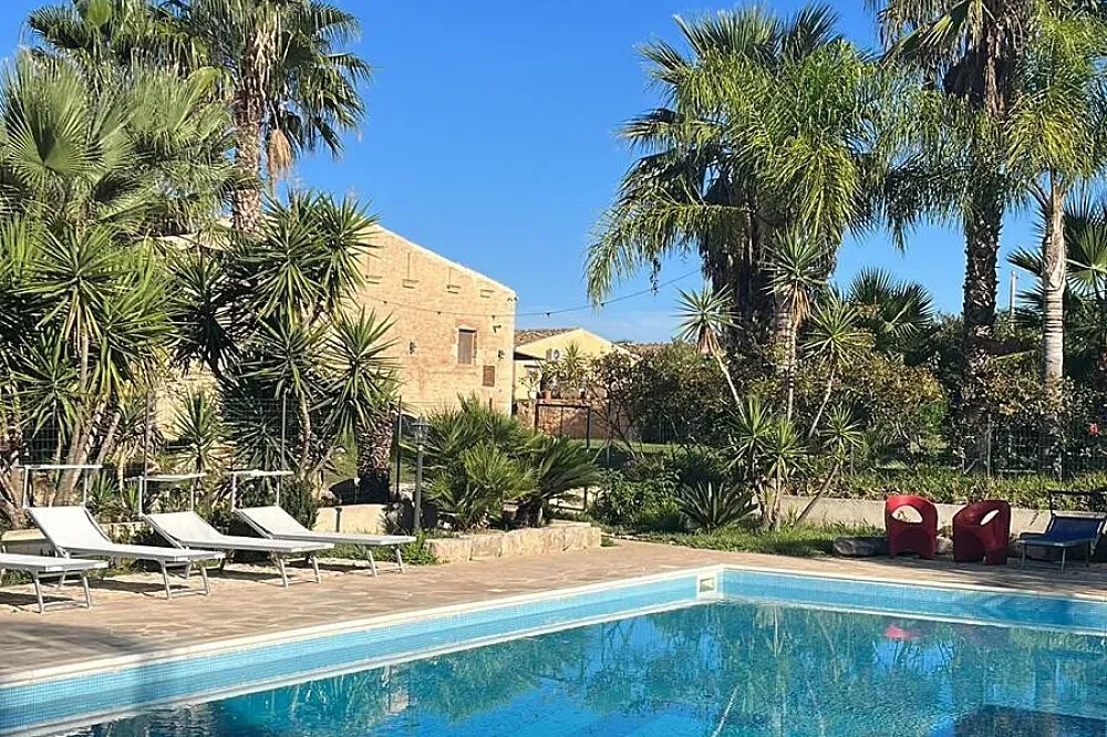 Masseria Boscorotondo — The Masseria is set within a vast garden landscape, dotted with mature palm, carob, and olive trees, creating a tranquil and verdant atmosphere. The property's proximity to the golden sandy beaches of Sicily's South coast means the refreshing sea air and coastal beauty are always within reach. The surrounding area is rich with historical Baroque cities, offering a blend of natural beauty and cultural immersion.