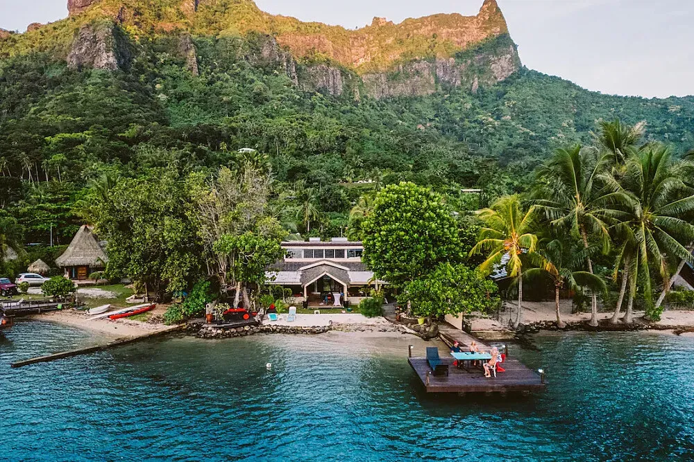 Private Beachfront Villa — The villa is situated directly on the stunning Cook's Bay in Moorea, offering immediate access to the turquoise waters. It's enveloped by vibrant tropical greenery, with the dramatic backdrop of volcanic mountains providing a majestic and serene atmosphere. The natural beauty of the location is a central part of the retreat experience.