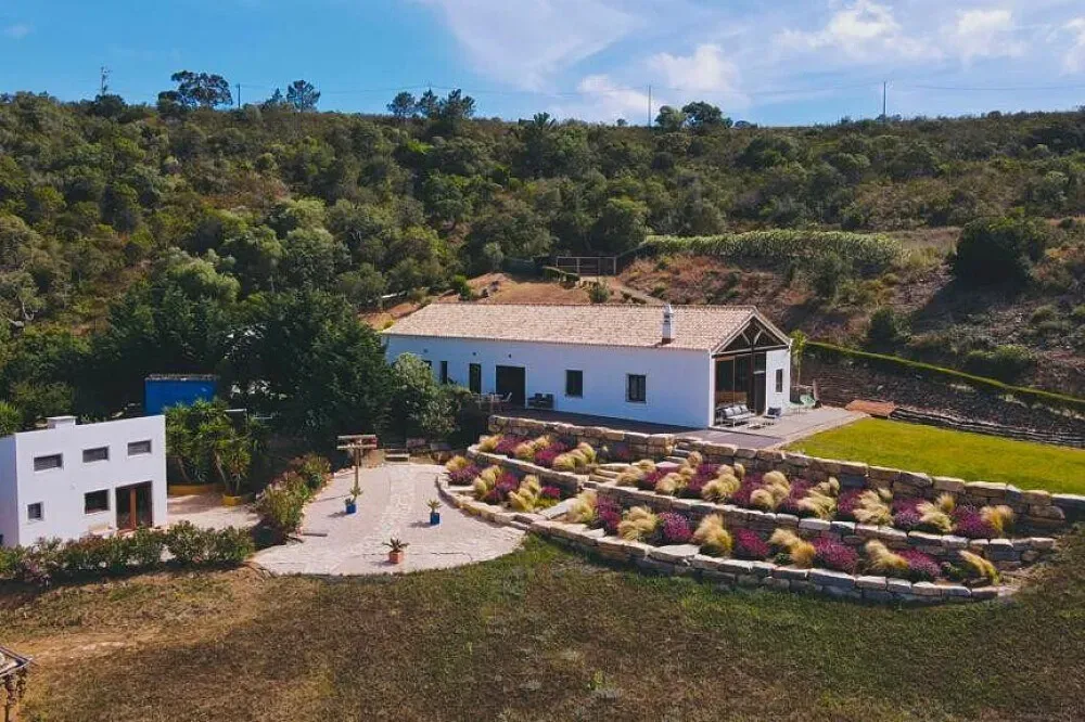 Salt House Portugal — The center is situated on a beautiful five-hectare property, immersed in nature. It boasts an infinity wooden yoga deck that offers breathtaking views of the Amoreira Valley and the distant ocean. The location provides direct access to the famous Costa Vicentina hiking trails and is just a short five-minute drive from the pristine surf beaches of Monte Clerigo, Amoreira, and Arrifana.
