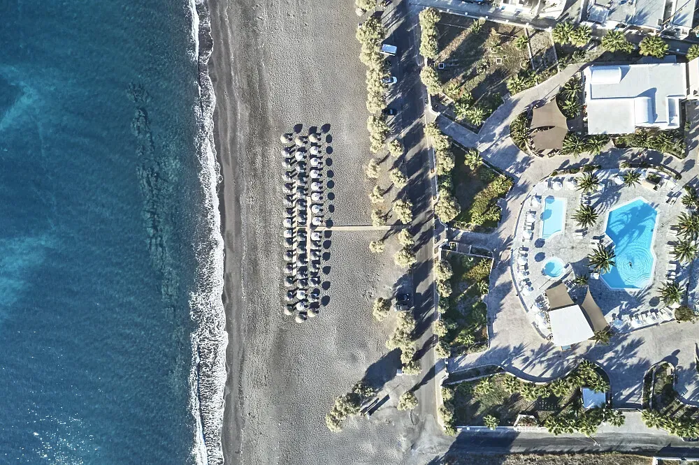 Santo Miramare Resort — The resort is perfectly situated on the black sandy beach of Perivolos, offering direct access to the unique volcanic coastline of Greece. The atmosphere is one of relaxed luxury, with the vibrant colors of the Aegean Sea and sky providing a stunning backdrop to your stay.