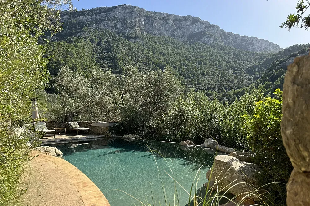 Son Rullan — Son Rullan is situated on a rugged Mallorcan mountaintop within the Serra de Tramuntana, surrounded by a landscape dotted with centuries-old olive trees. The property boasts a semi-wild garden and offers stunning Mediterranean views, creating an atmosphere of historical grandeur and natural tranquility.