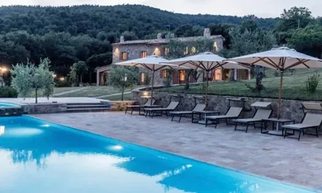 A Tuscan Rebirth: Female Power — The retreat unfolds in the serene Tuscan countryside, about 1.5 hours from Florence. The atmosphere is one of expansive golden landscapes, inviting guests to connect with nature's beauty and tranquility. A large villa with an infinity pool serves as the central hub, offering a luxurious and relaxing environment.