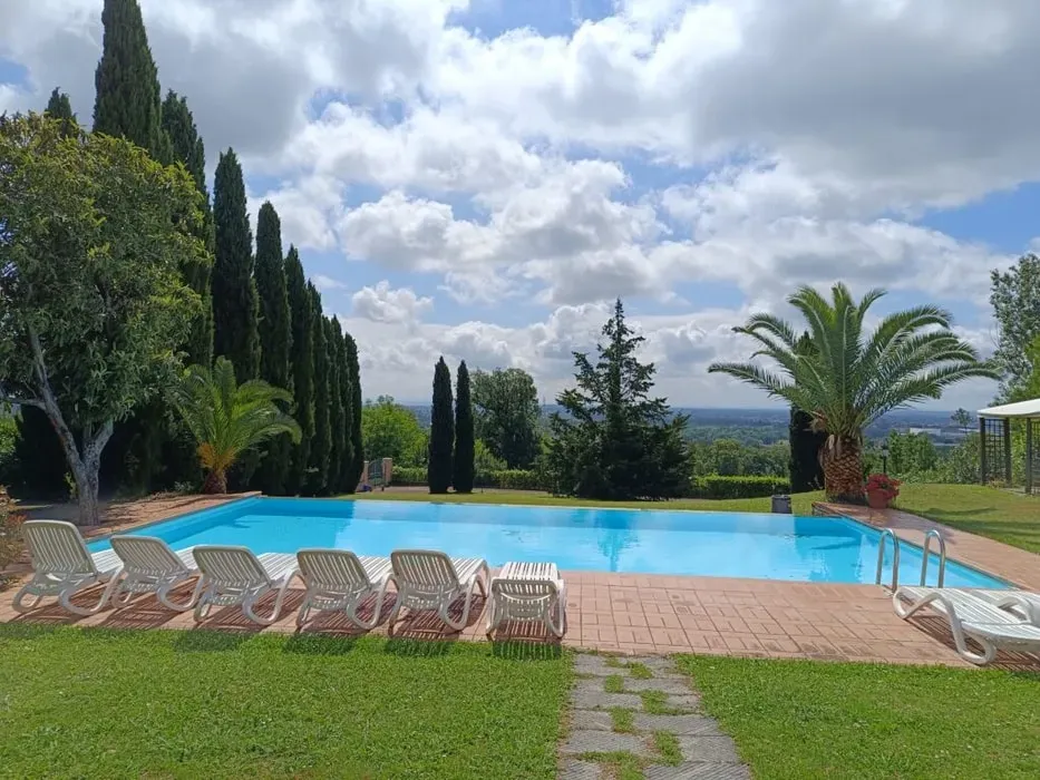 Barbagianni Retreats & Events — set in the picturesque Tuscan countryside near Lucca, the retreat is surrounded by 1.5 hectares of gardens offering views of distant hills and mountains. The atmosphere is one of serene relaxation, with cypress trees lining the private infinity pool and mimosa trees providing shade for outdoor yoga sessions. Dining takes place under a charming covered pergola, enhancing the Mediterranean experience.