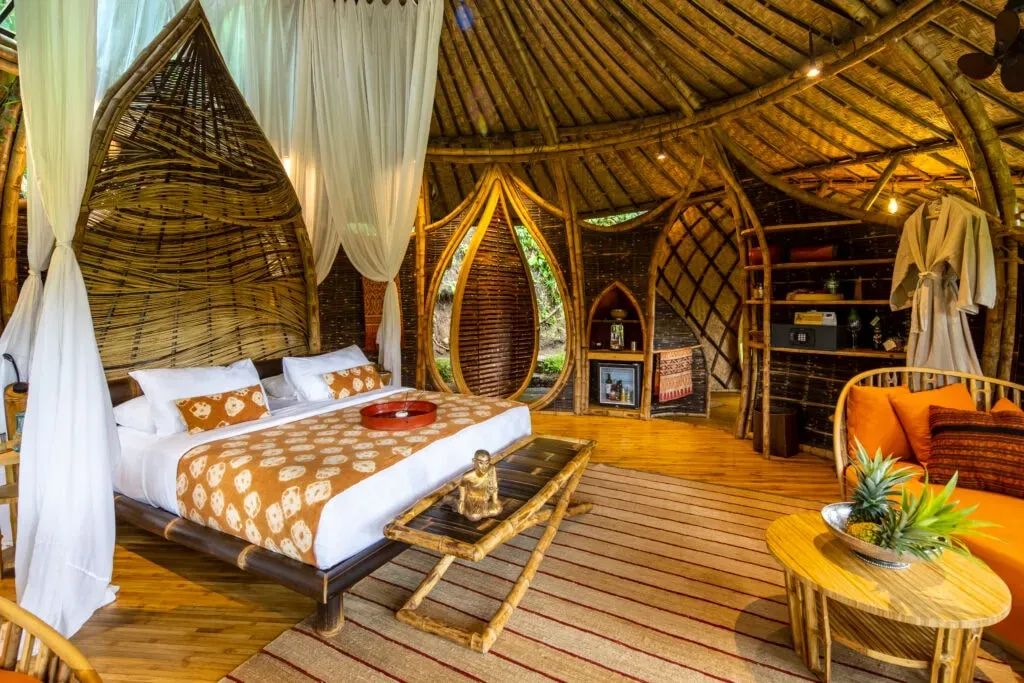 Dr. Himani Barot — set in the heart of Ubud's lush jungle, Bambu Indah provides an eco-luxury sanctuary. Handcrafted bamboo and wooden houses offer open-air bathrooms and serene river views. Natural spring water pools, a jungle yoga deck, and riverside meditation spaces are integrated into the landscape, fostering a deep connection with nature.