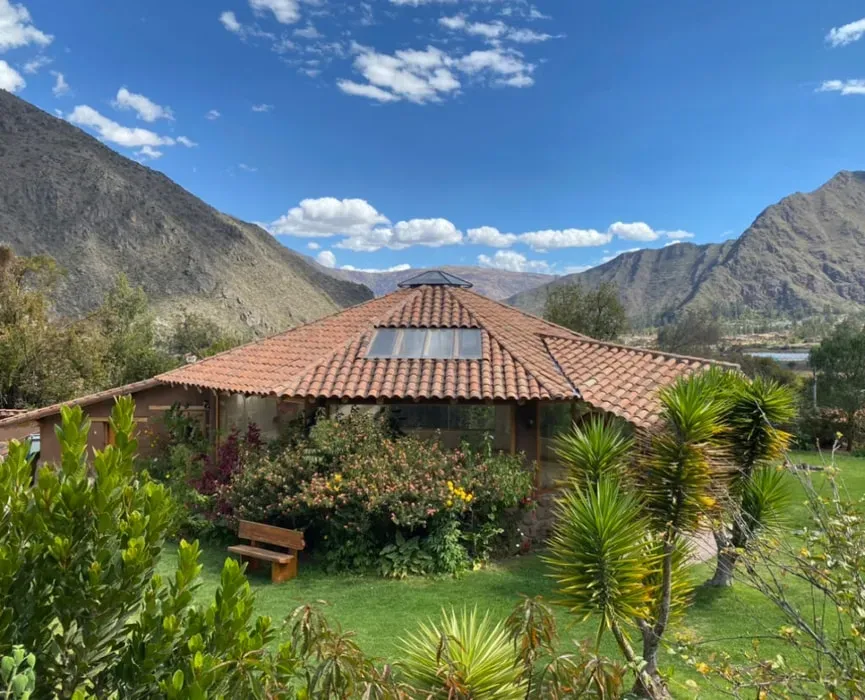 Intertwining Medicines — set 90 minutes from Cusco in the mystical Sacred Valley of Peru, the venue is a vibrant oasis. Lush gardens burst with color, creating a serene and relaxing atmosphere. Everywhere you look, jagged Andean mountain peaks pierce the sky, even visible from the maloka-style yoga studio. Guests can unwind by the pool or sway gently in hammocks, soaking in the breathtaking views.