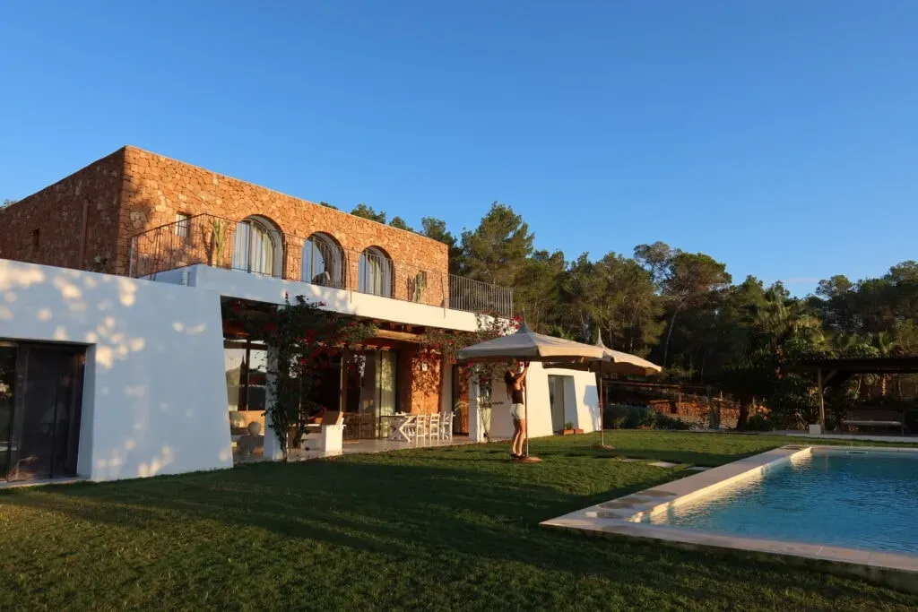 Kakun — Perched on a hill in the heart of Ibiza, Cas Fale is a stunning private villa surrounded by the island's natural beauty. The atmosphere is one of intentional cultivation for well-being, with spaces designed for both active practice and serene relaxation. The afternoon light casts a golden glow, enhancing the peaceful and beautiful environment.