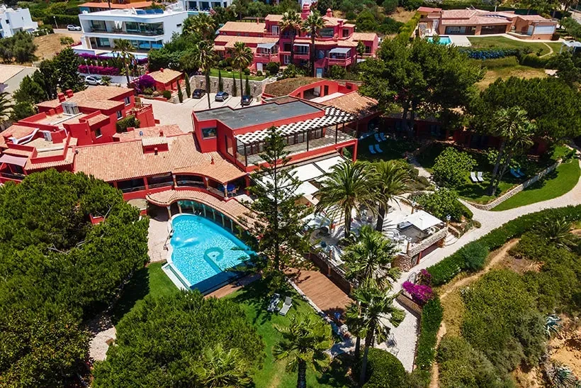 Wellness Waves and Wine — Perched dramatically on a cliff overlooking the beautiful Porto do Mos beach in Lagos, southern Portugal, the setting is one of serene coastal beauty. Lush, carefully landscaped gardens surround the boutique hotel, providing tranquil spaces to relax, all against the backdrop of the sparkling ocean.